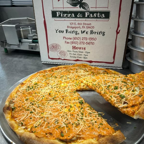 A Dino's Pizza & Pasta pizza with orange sauce, cheese, and herbs, with a box in the background.
