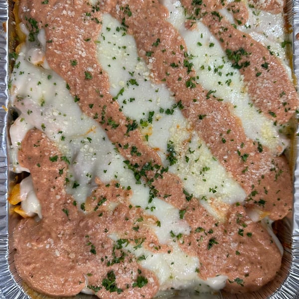 Baked pasta with melted white cheese, pink sauce, and green herbs in a foil container.