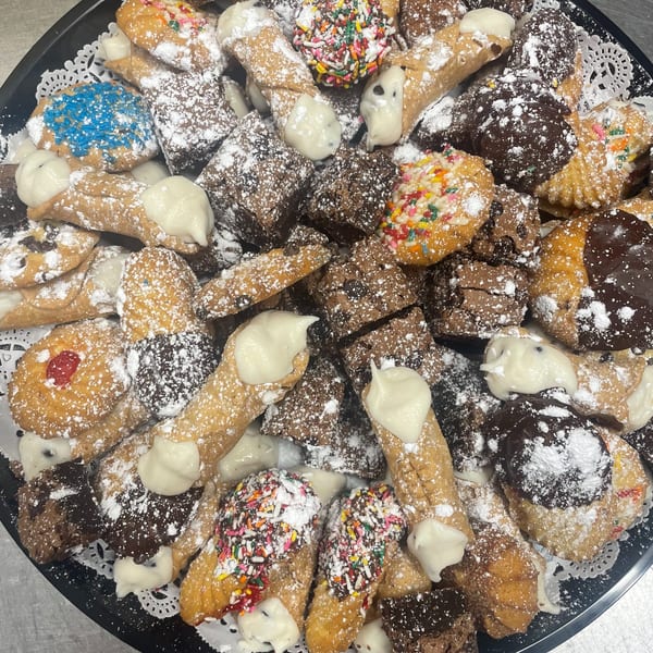 A platter of Dino's Pizza & Pasta's Italian pastries, including cannolis, cookies, and brownies, dusted with powdered sugar.