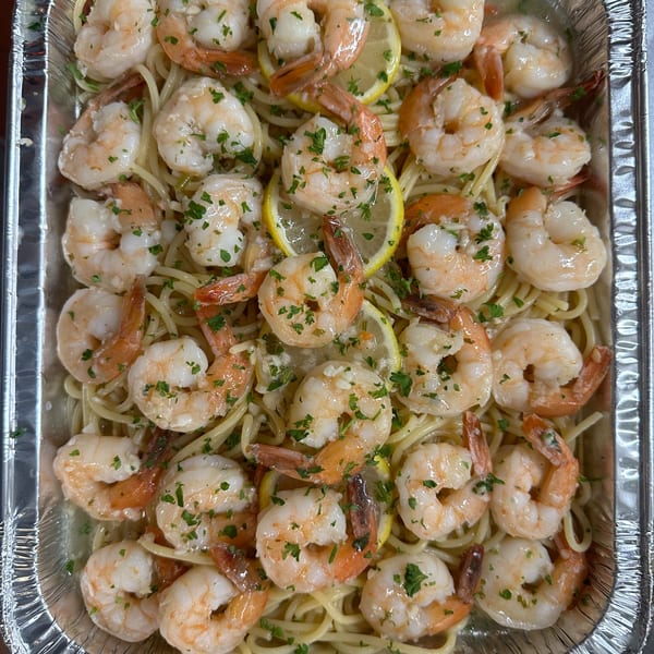 Shrimp scampi with pasta, lemon slices, and parsley in a foil take-out container.