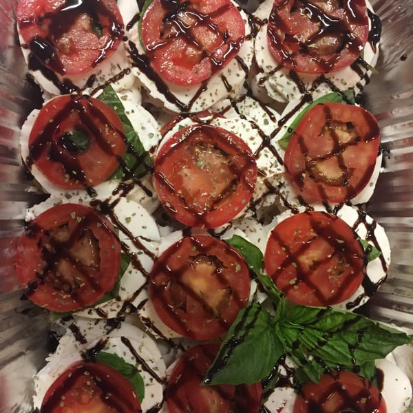 Caprese salad with sliced tomatoes, mozzarella, basil, and balsamic glaze in a foil tray.