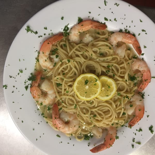 Shrimp scampi with spaghetti, lemon slices, and parsley on a white plate.