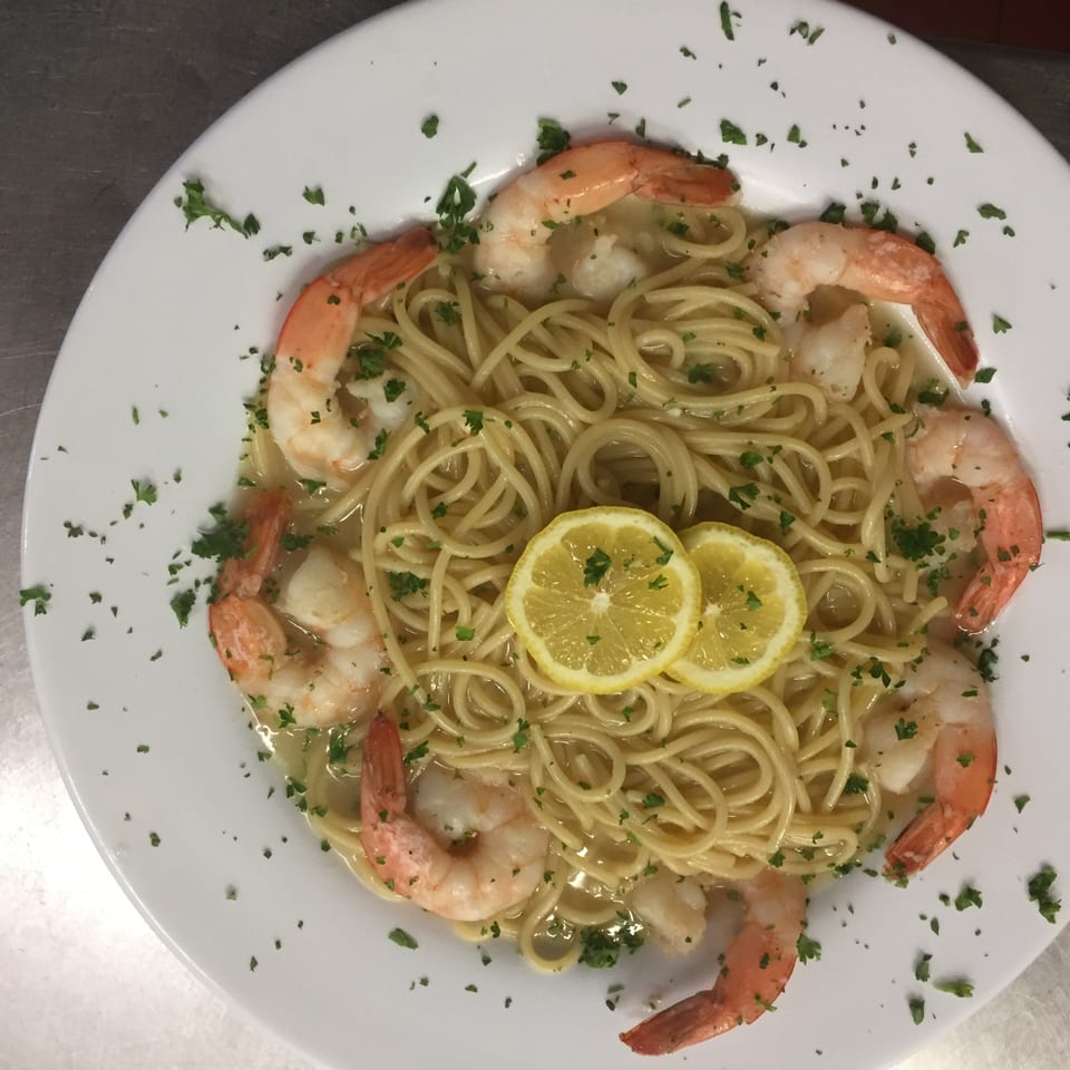Shrimp scampi with spaghetti, lemon slices, and parsley on a white plate.