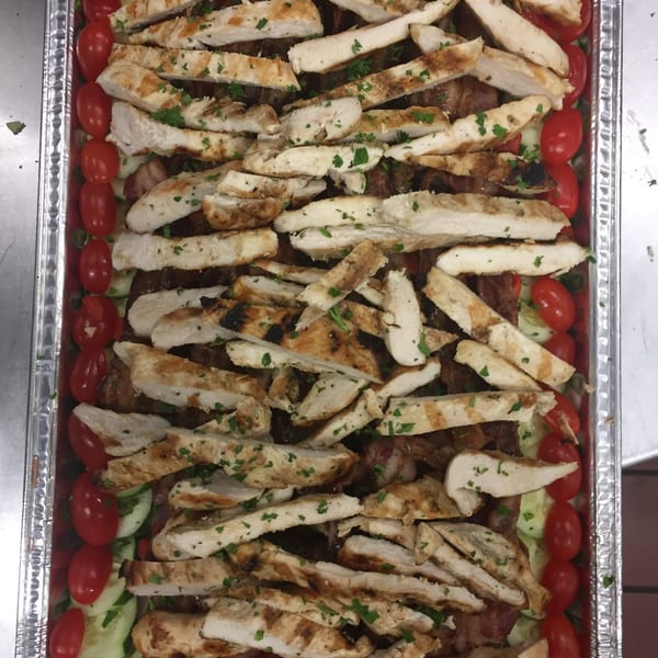 Grilled chicken strips, cherry tomatoes, and cucumbers in a catering tray from Dino's Pizza & Pasta.