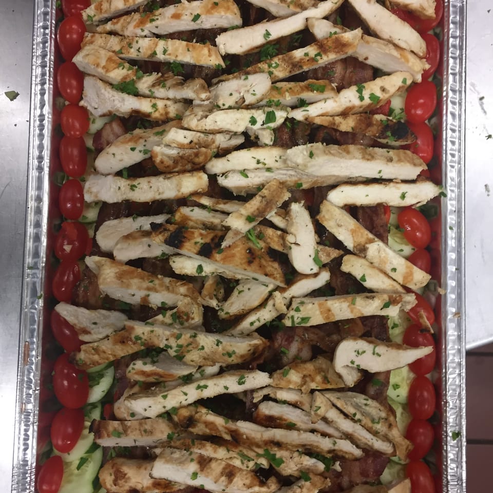 Grilled chicken strips, cherry tomatoes, and cucumbers in a catering tray from Dino's Pizza & Pasta.